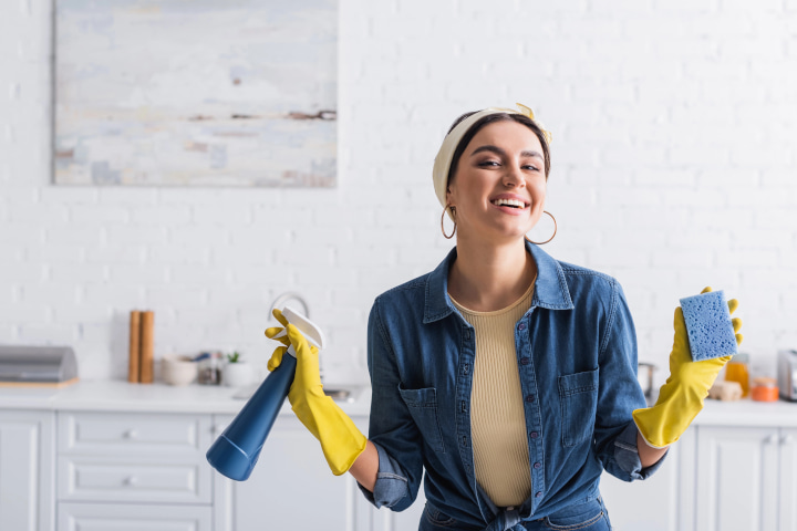 Smiling female cleaner in rubber gloves holding sponge and detergent — Photo