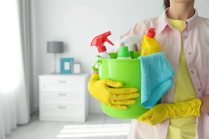 Woman holding bucket with different cleaning supplies